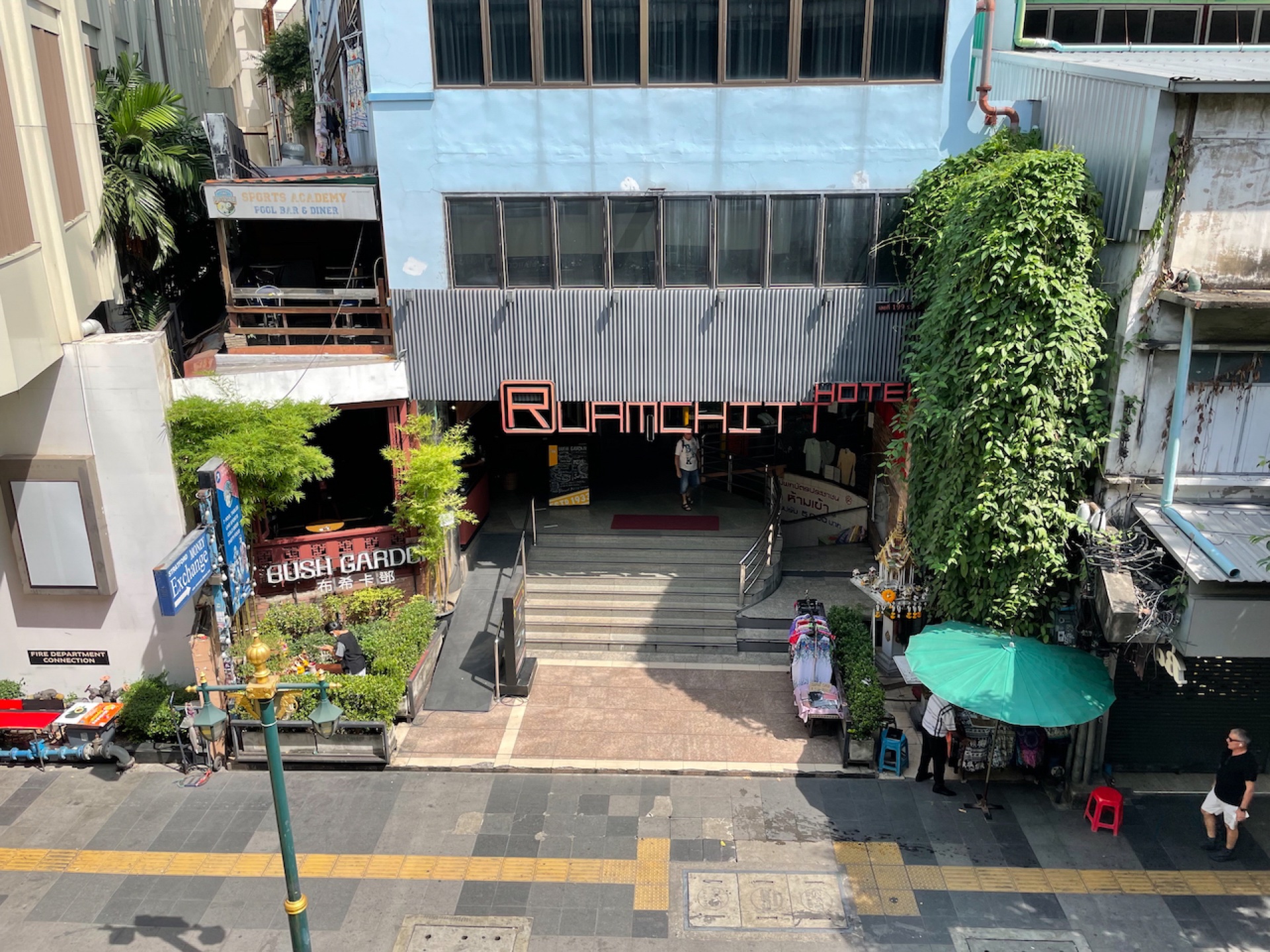 Eingang eines Hotels an einer Sukhumvit-Seitenstraße mit begrüntem Gebäude und Straßenständen