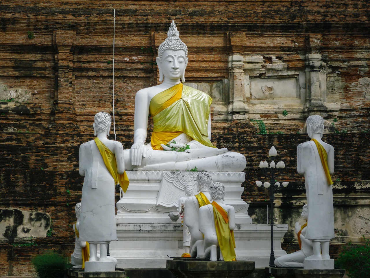 Weiße Buddhafiguren vor einer alten Backsteinmauer in Ayutthaya
