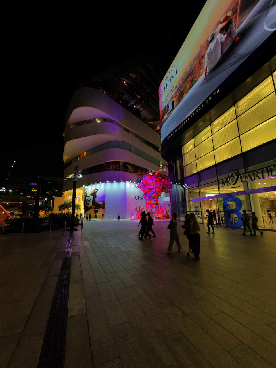 EmQuartier Einkaufszentrum bei Nacht – moderne Architektur, bunte Skulptur und Flaneure vor dem Eingang