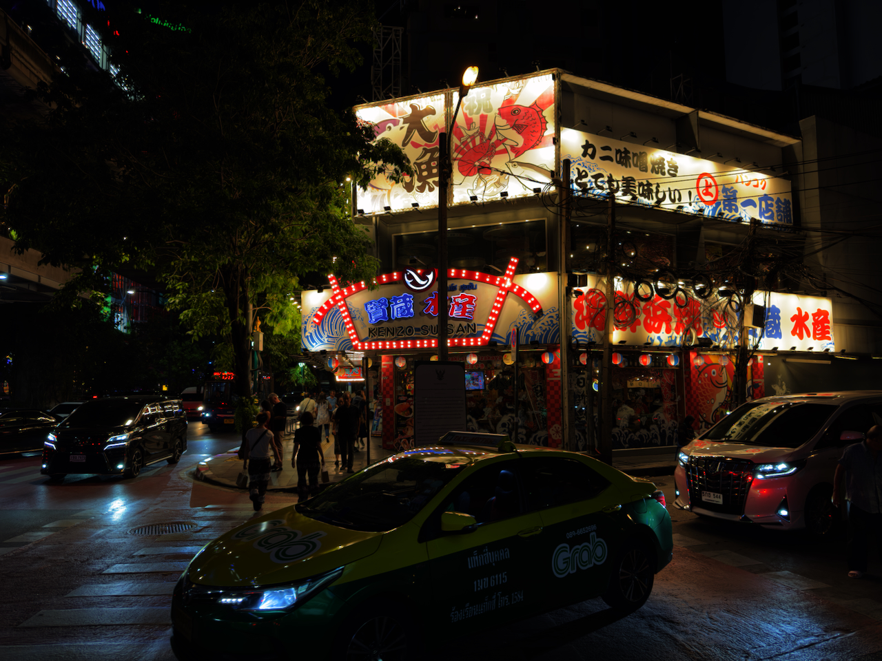 Japanisches Restaurant mit leuchtenden Kanji-Neon-Schildern in Thonglor bei Nacht – Grab-Taxi im Vordergrund