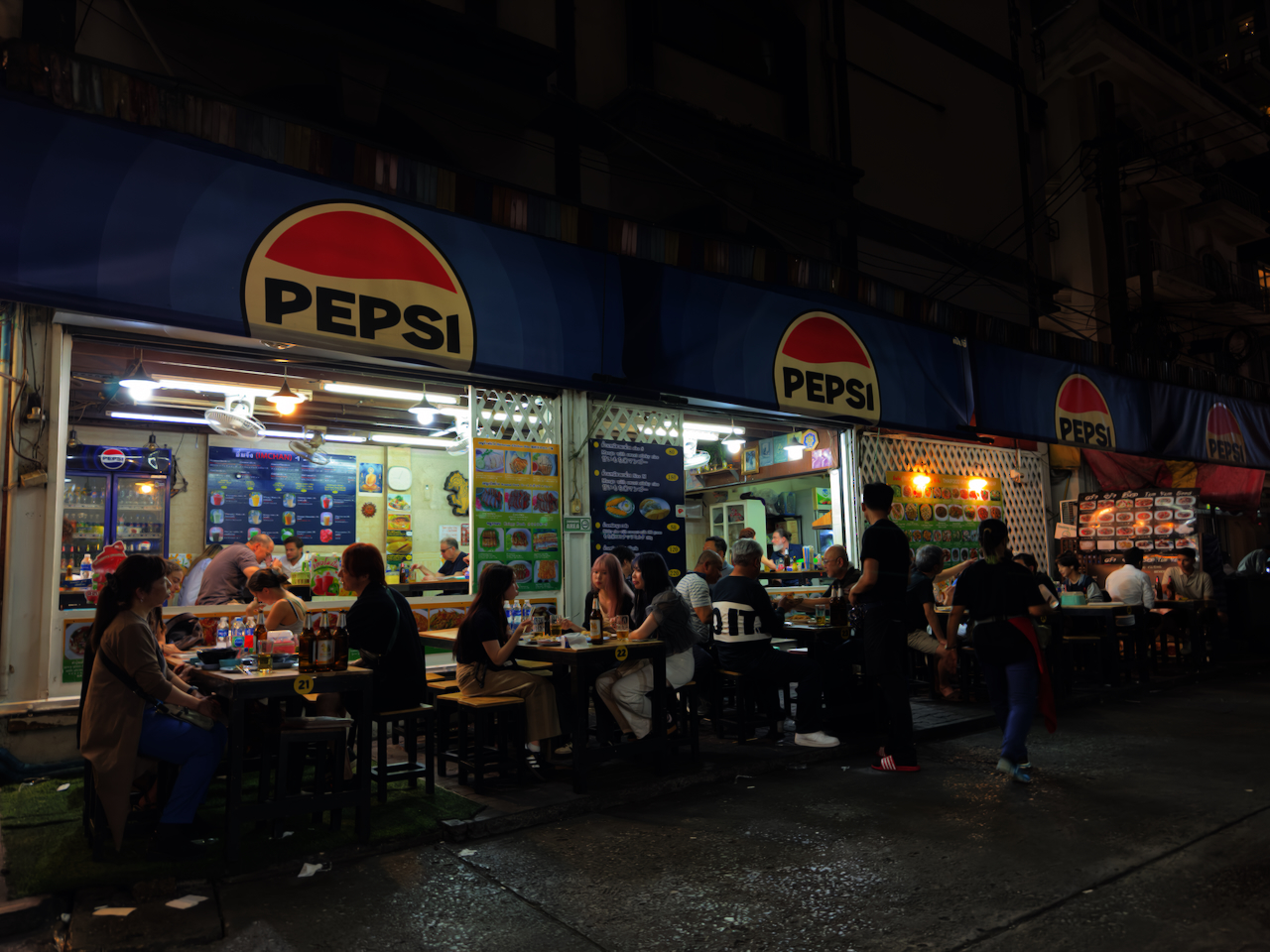 Abendliche Garküchen mit Pepsi-Schildern in Thonglor – viele Gäste beim Streetfood-Dinner auf dem Gehweg