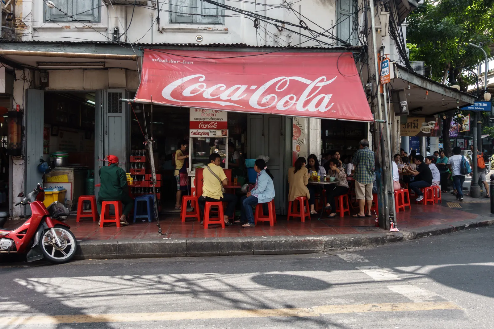 Streetfood-Ecke in Bangkok mit roten Plastikhockern und einzelnen Gästen