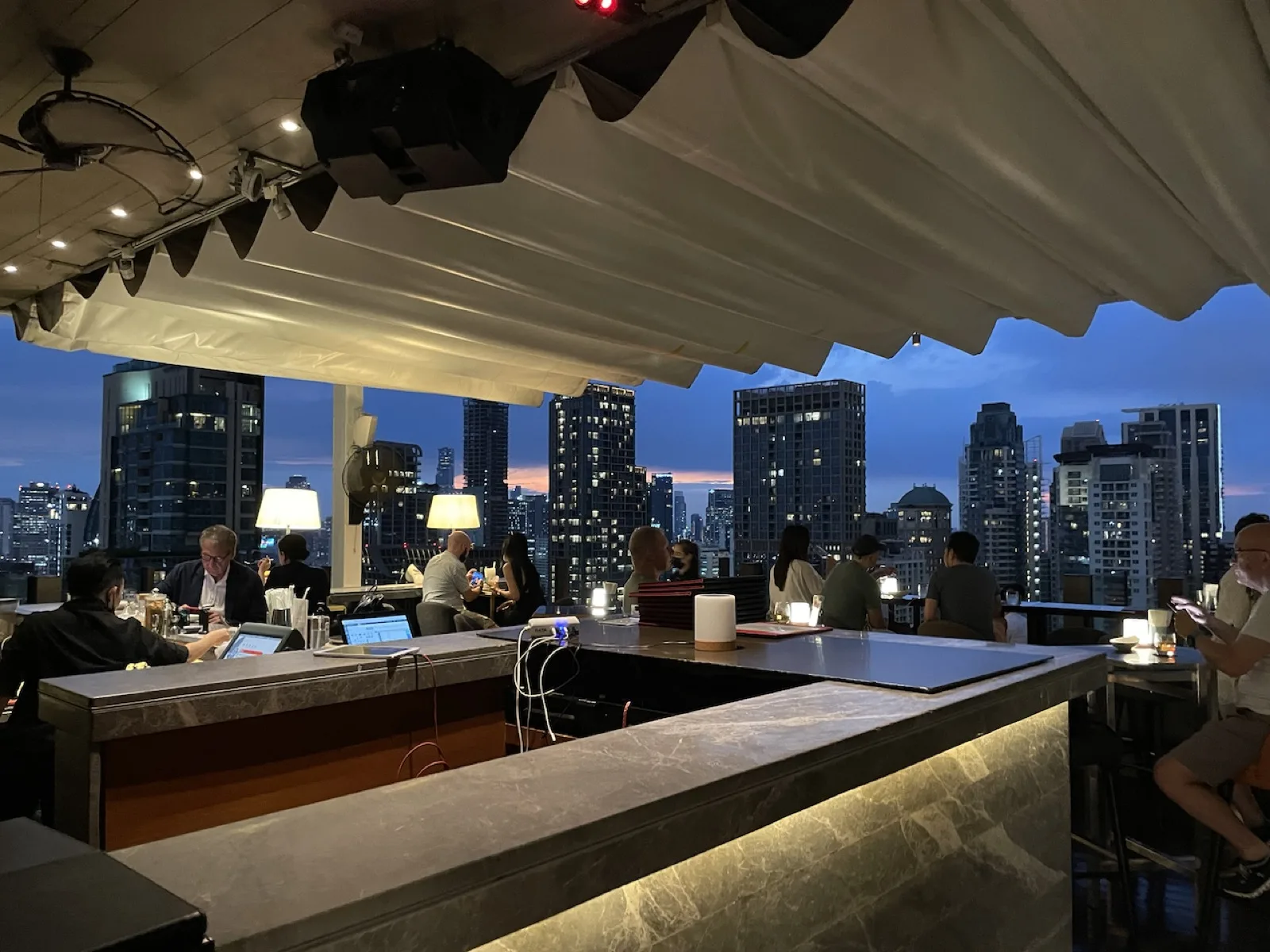 Blick von einer Rooftop-Bar auf die beleuchtete Skyline von Bangkok bei Nacht