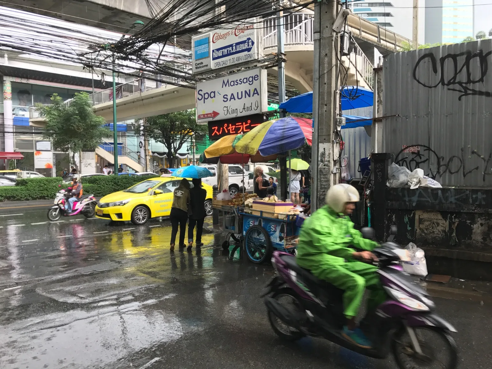 Monsunregen auf einer Straße in Bangkok mit Rollerfahrer im Regenponcho