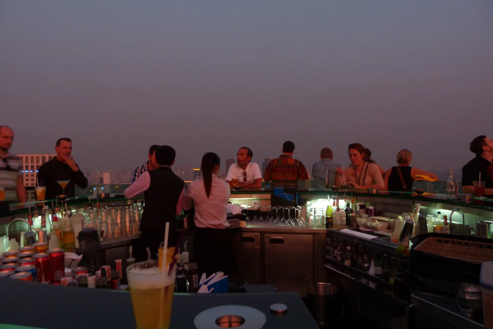 Bar-Tresen einer Rooftop-Bar in Bangkok mit Cocktails und Barkeepern in der Abenddämmerung