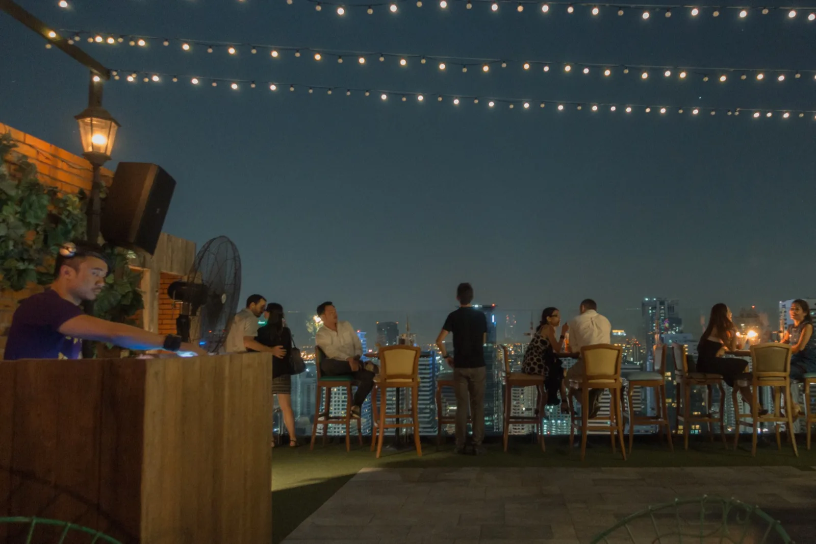 Rooftop-Bar-Terrasse in Bangkok mit Lichterketten und Gästen vor der abendlichen Skyline