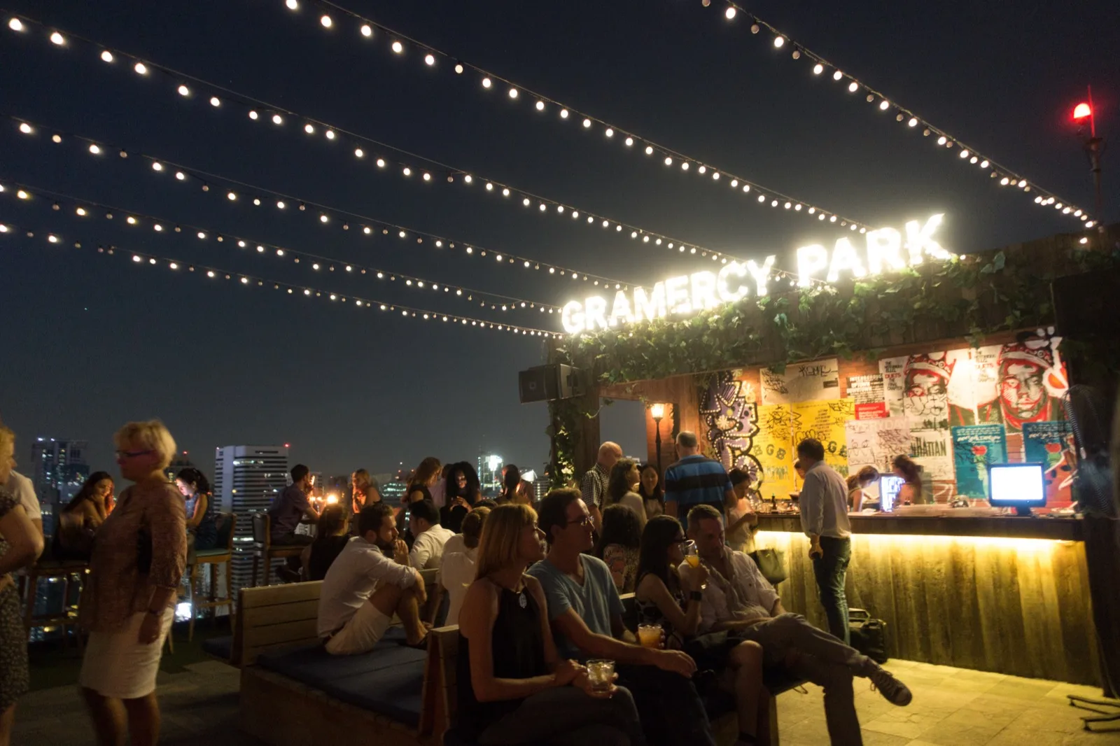 Reisende unterhalten sich abends an einer Rooftop-Bar in Bangkok unter Lichterketten