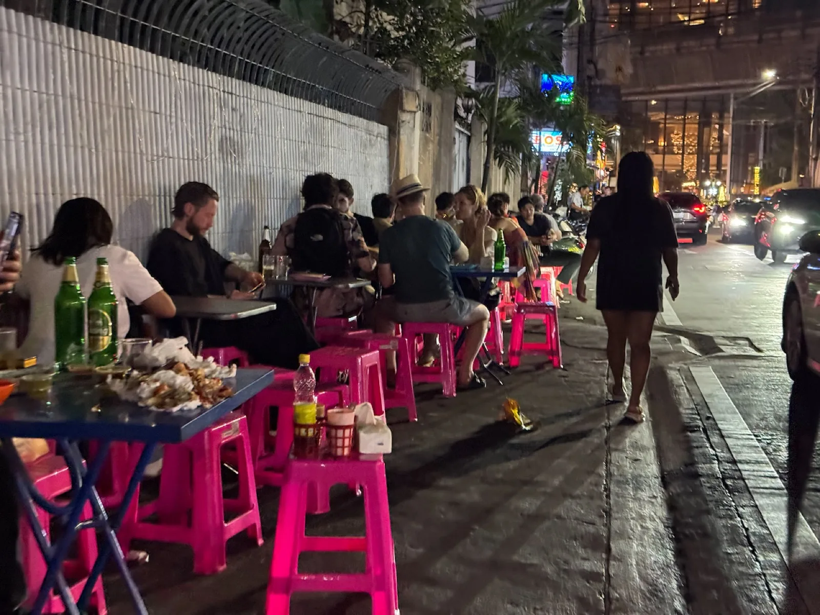 Gäste an Straßenküchen-Tischen mit pinken Plastikhockern am Abend in Bangkok