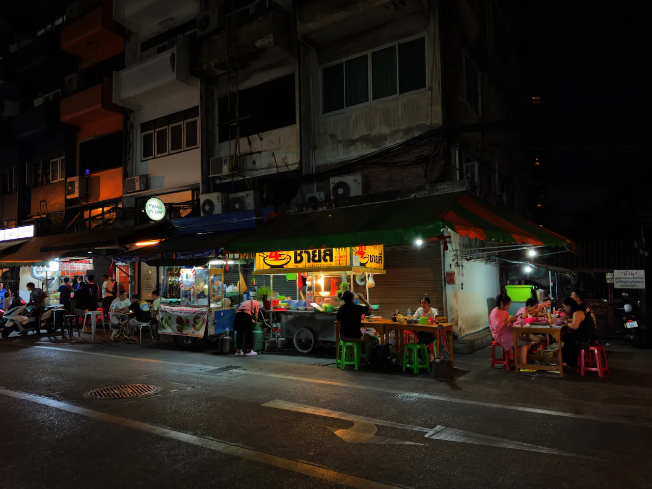 Nächtliche Streetfood-Stände mit Tischen und Hockern auf dem Gehweg in Bangkok