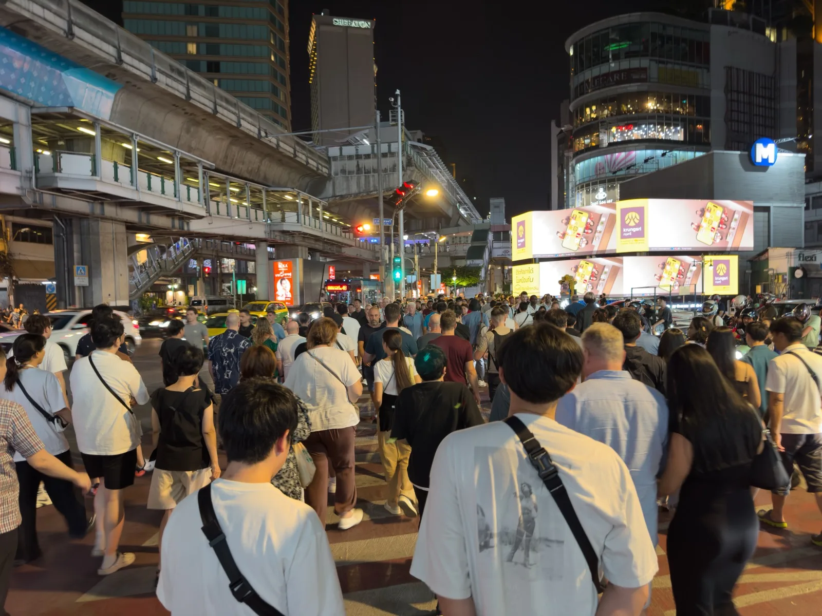 Belebte Asok-Kreuzung an der Sukhumvit bei Nacht mit BTS-Trasse und Menschenmengen