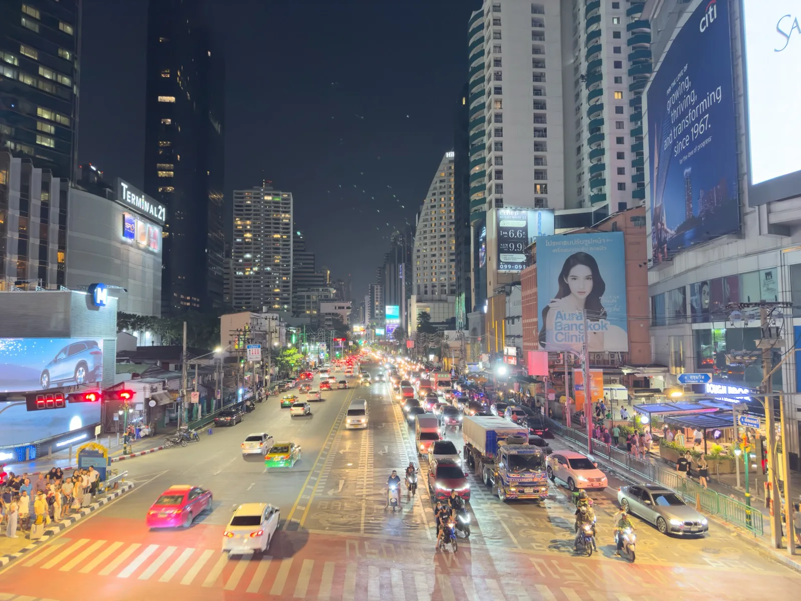 Hell erleuchtete, belebte Sukhumvit Road in Bangkok bei Nacht mit Verkehr und Fußgängern