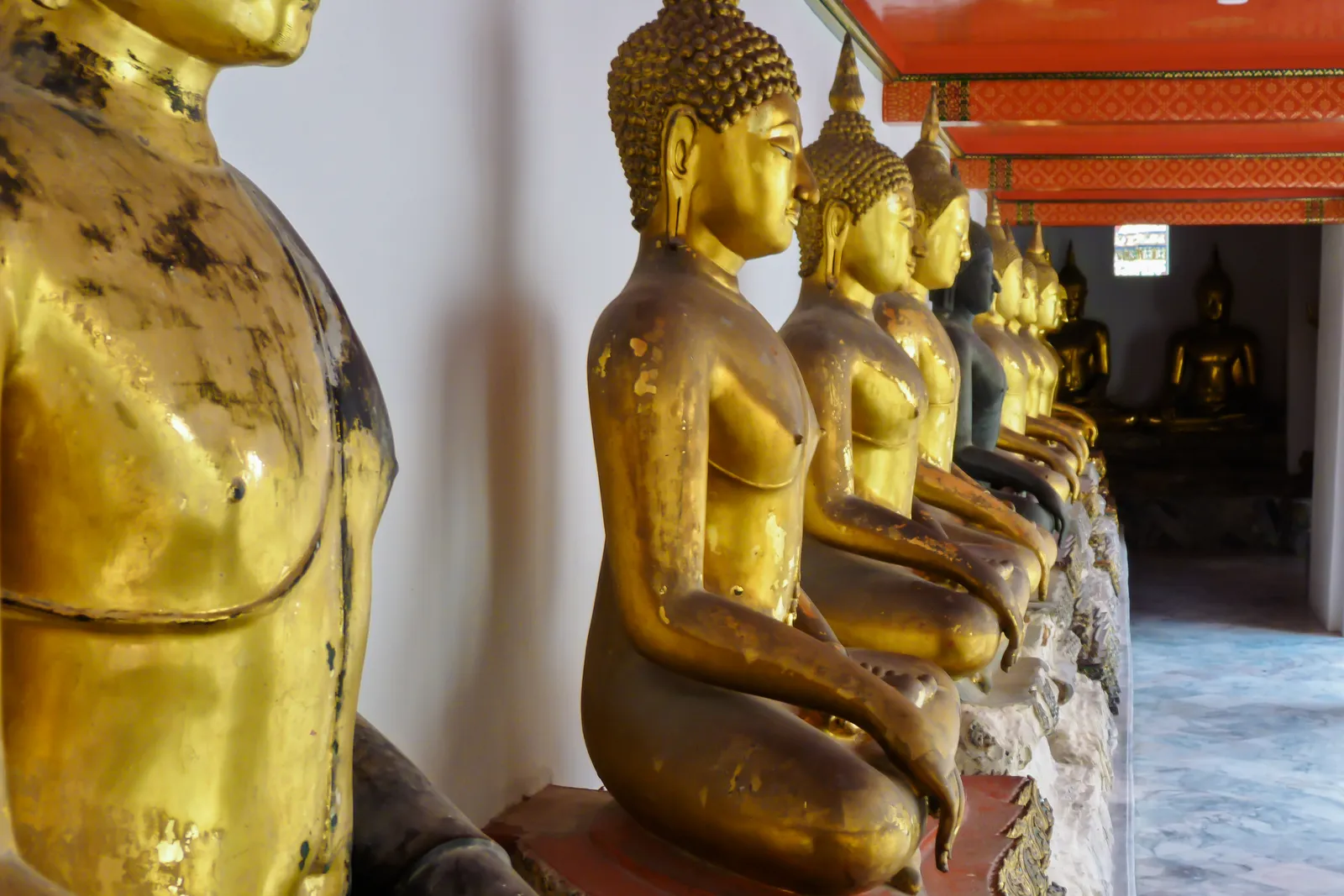 Reihe goldener Buddha-Statuen in einer Galerie des Wat Pho, Bangkok