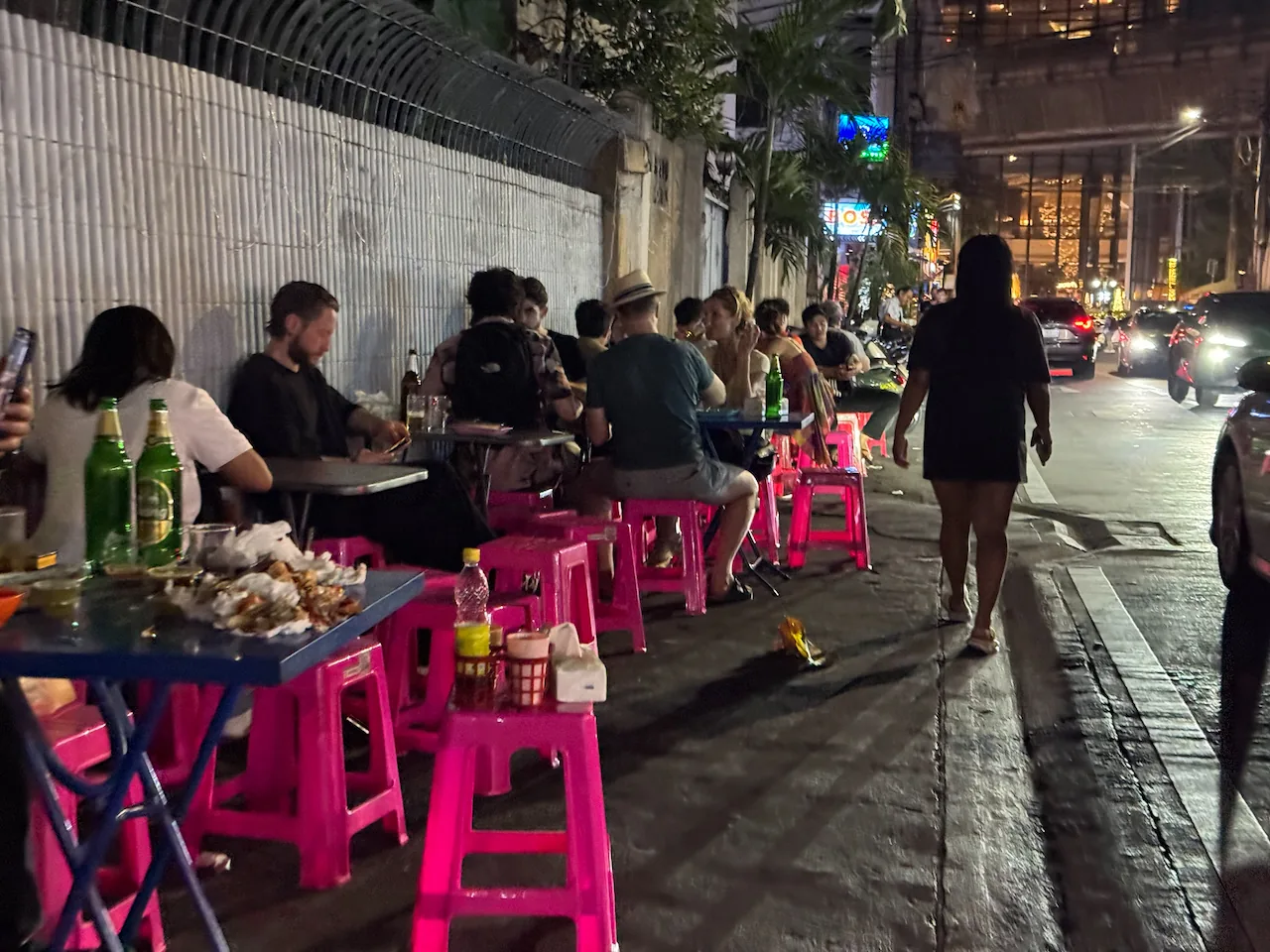 Gäste auf pinken Plastikhockern an Straßenständen in Bangkok am Abend