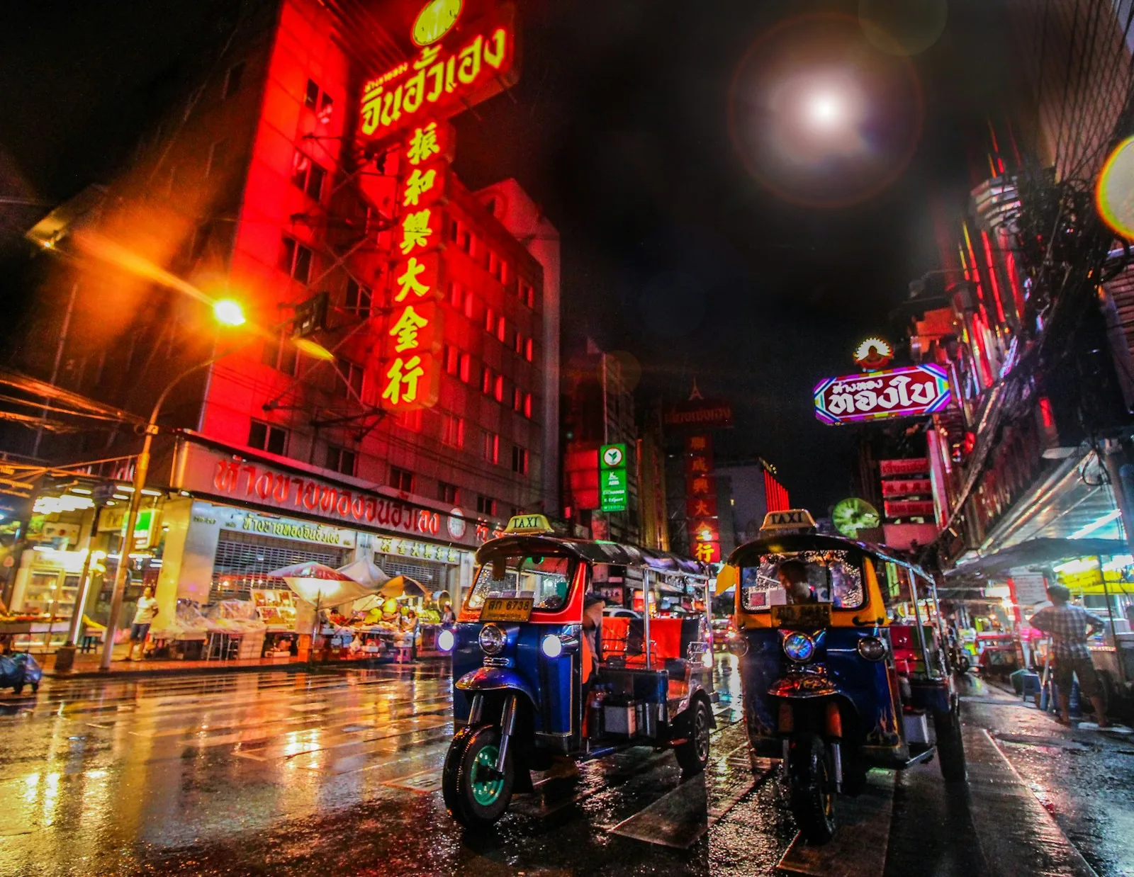 Abendmarkt in Bangkok nach dem Regen, nasse Straße glänzt, Straßenlaternen und Essensstände