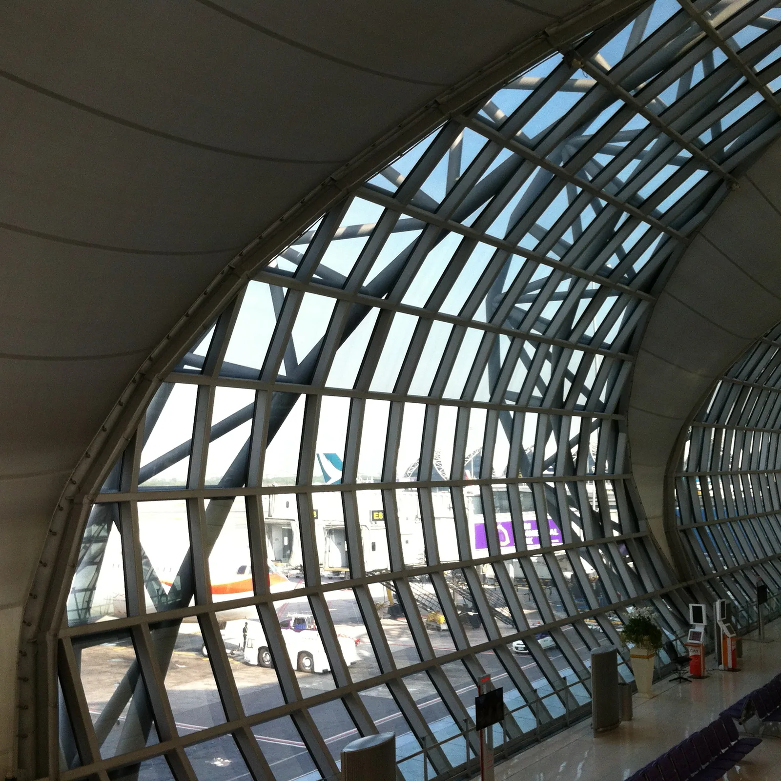Blick durch die hohe Glasfassade des Flughafens Suvarnabhumi auf das Vorfeld