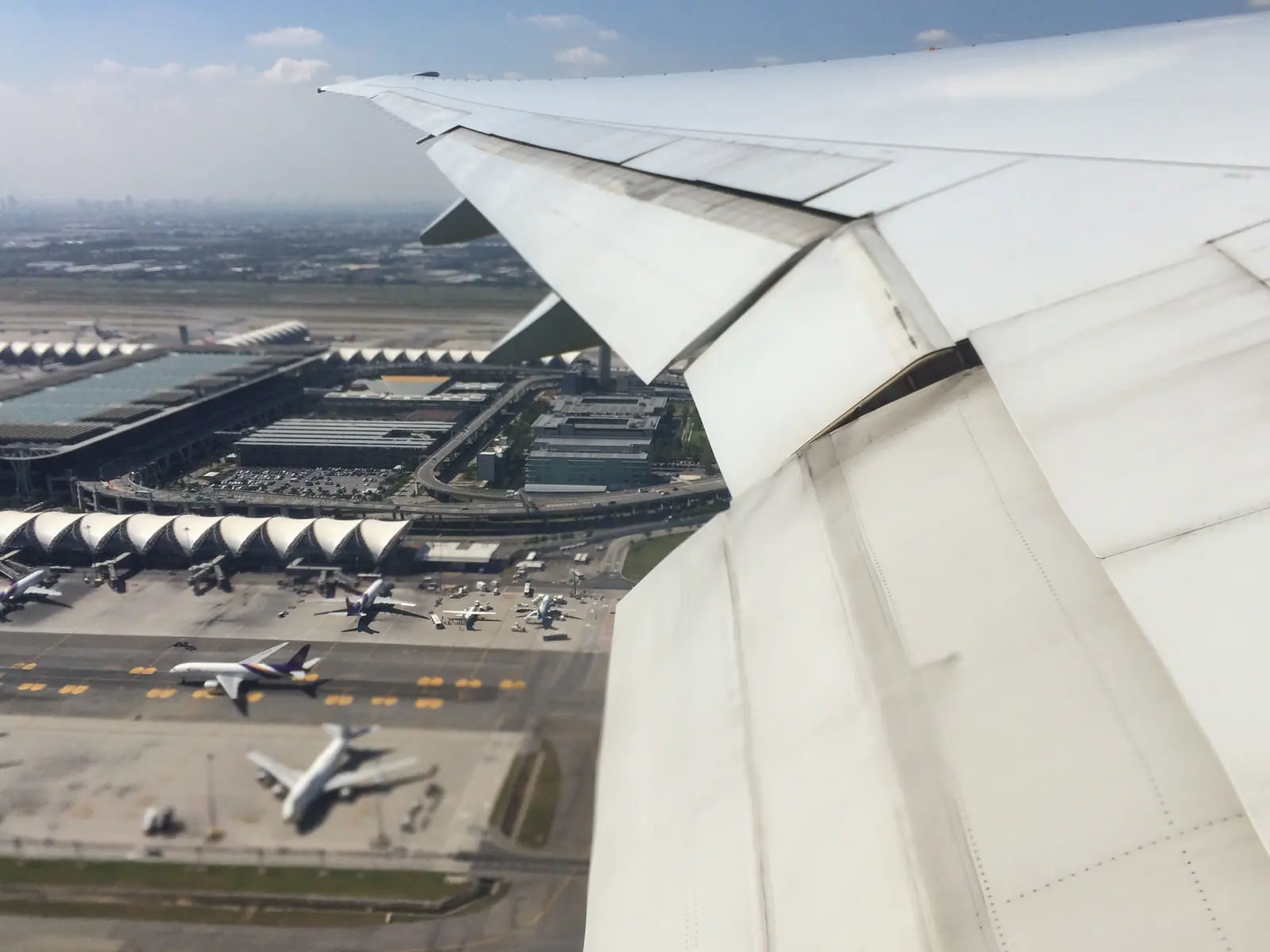 Blick aus dem Flugzeugfenster über die Tragfläche auf Vorfeld und Terminals des Flughafens Suvarnabhumi in Bangkok