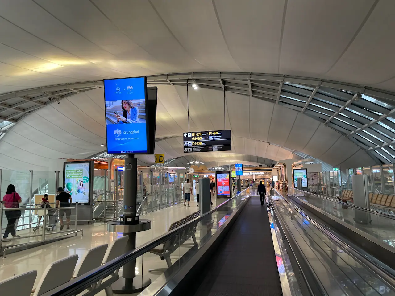 Terminalgang im Flughafen Suvarnabhumi mit Laufband, Infobildschirm und Wegweisern zu den Gates