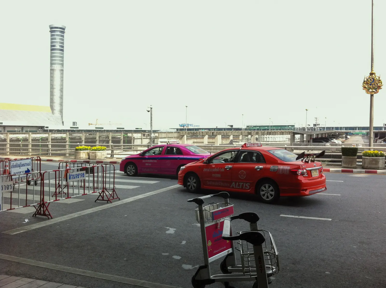 Taxis und ein Gepäckwagen an der Vorfahrt des Flughafens Suvarnabhumi, im Hintergrund der Kontrollturm